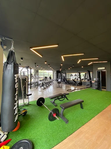 The gym floor at SSF Telok Panglima Garang: a punching bag, benches and a barbell on green turf, with cardio and strength machines behind.